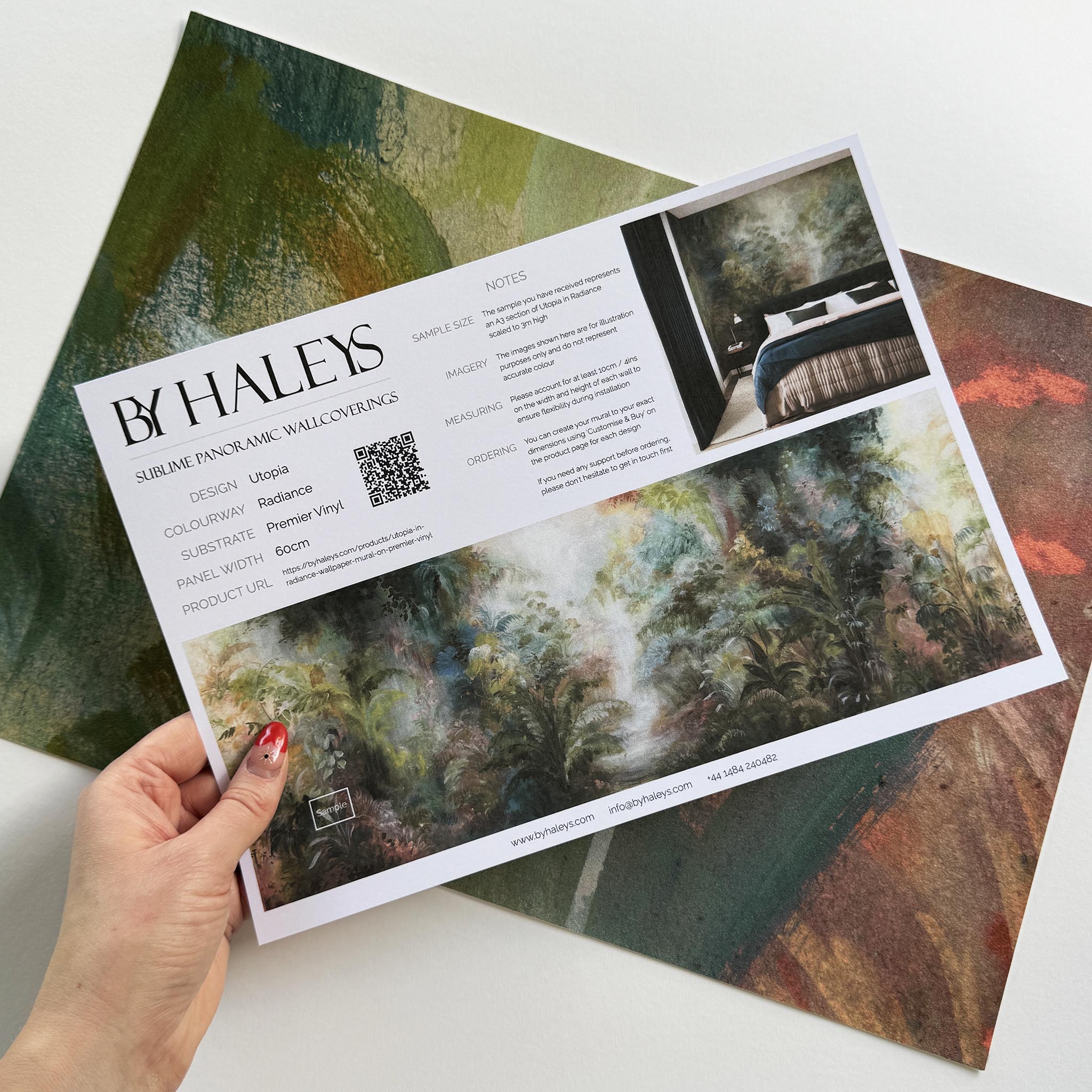 A hand showing information for a vinyl wallpaper mural sample which features a rainforest in green, coral, and gold.