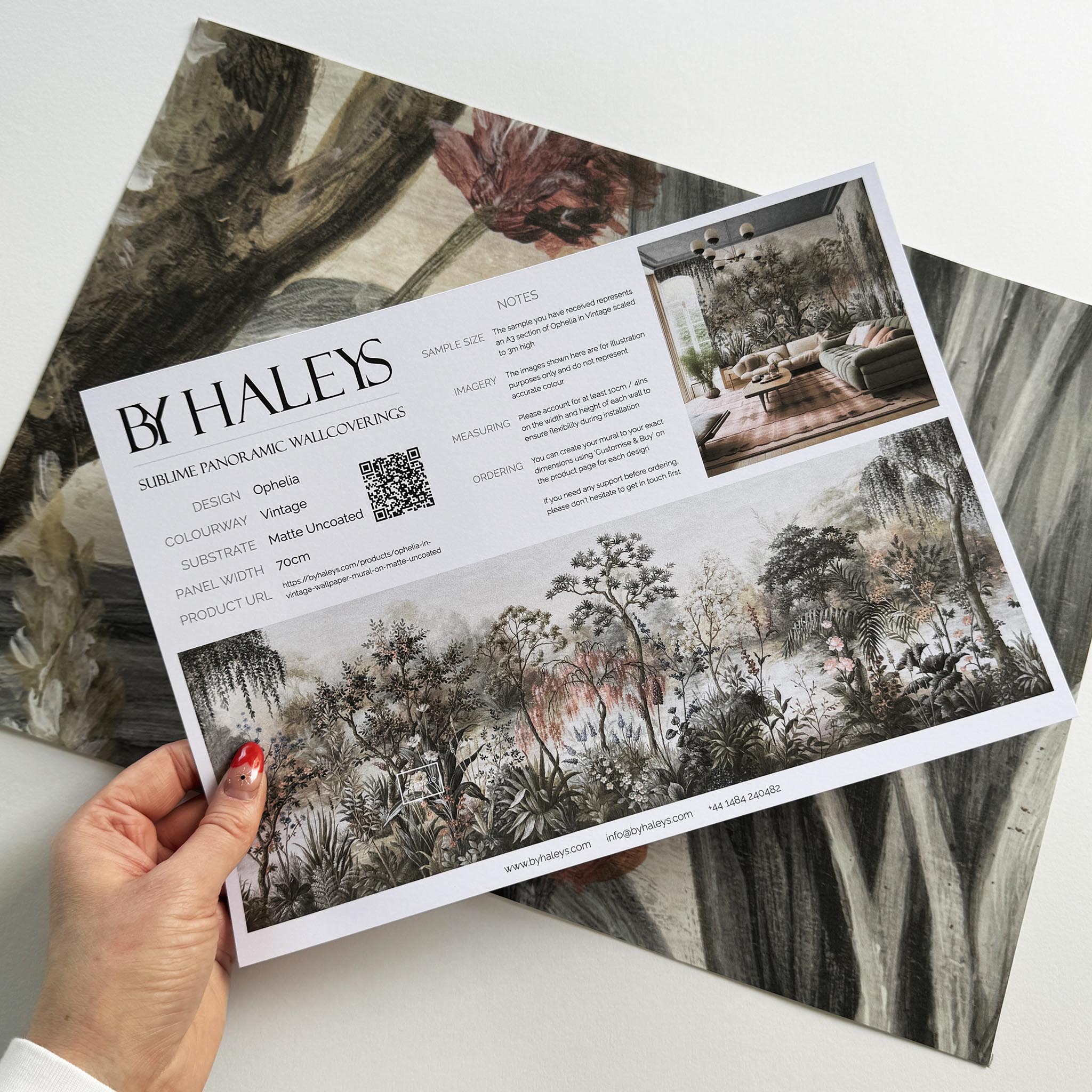A hand showing information for a matte wallpaper mural sample which features a lakeside scene in vintage tones.