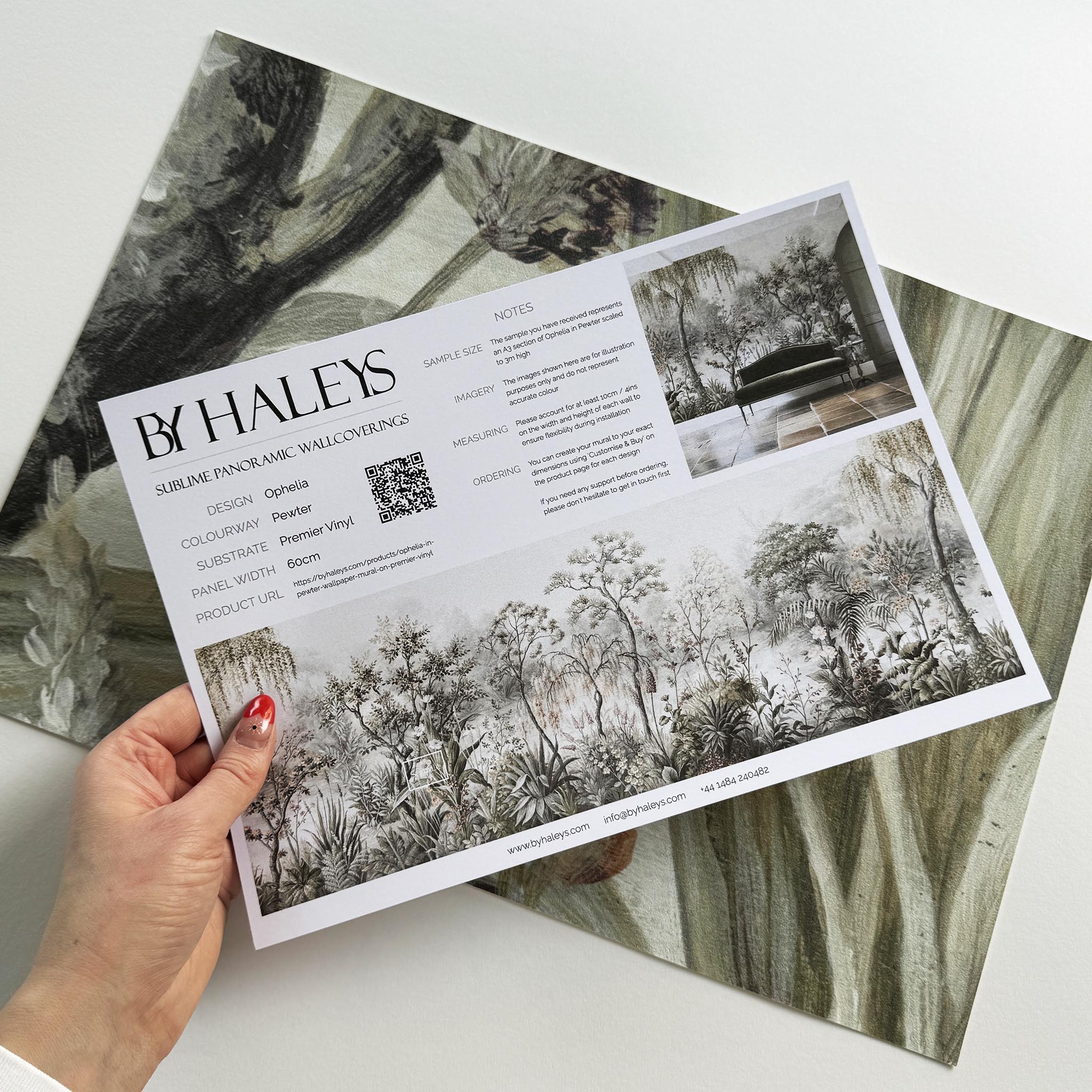 A hand showing information for a vinyl wallpaper mural sample which features a lakeside scene in grey and peach.