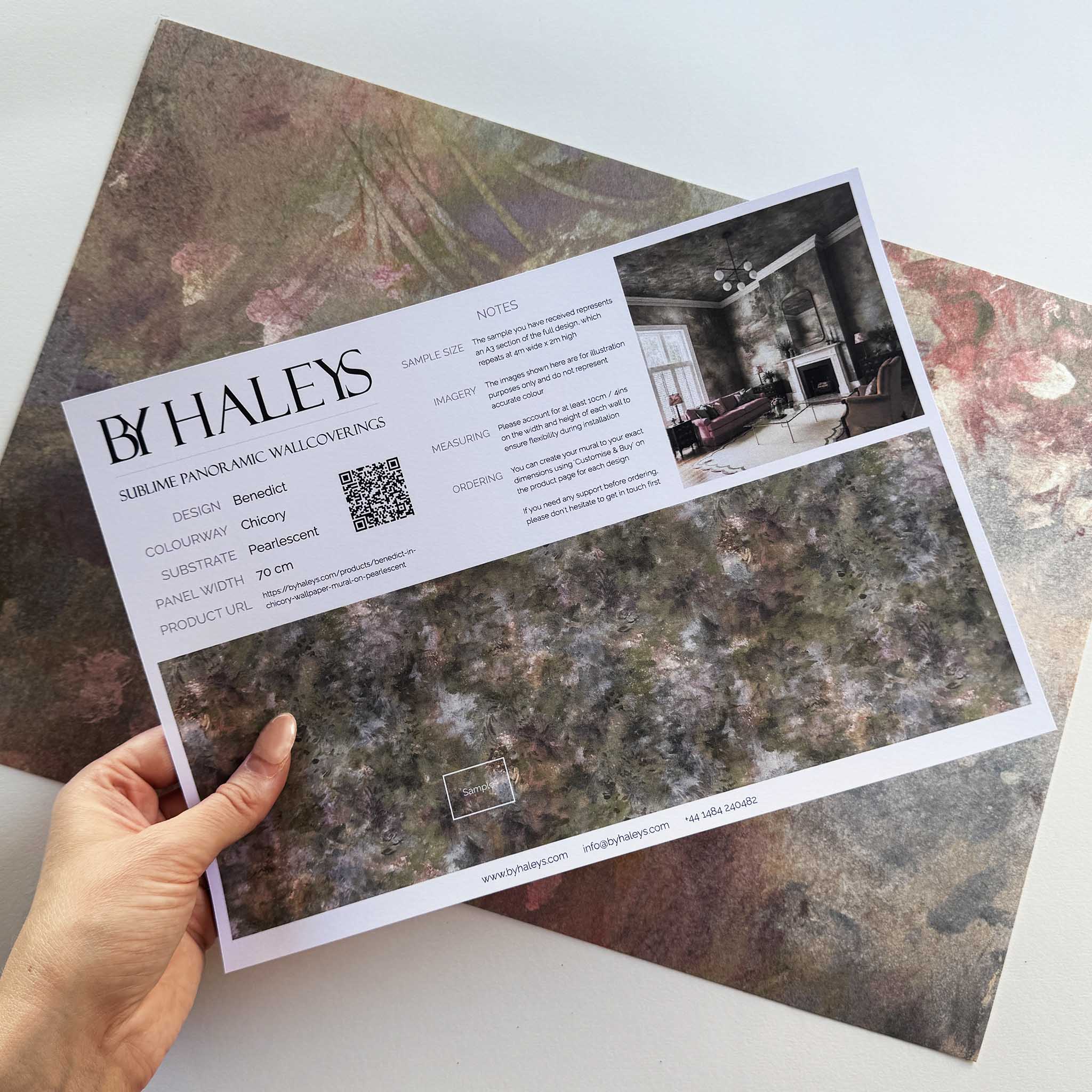 A hand showing information for a pearlescent wallpaper mural sample which features muted botanical interior mural in shadow.