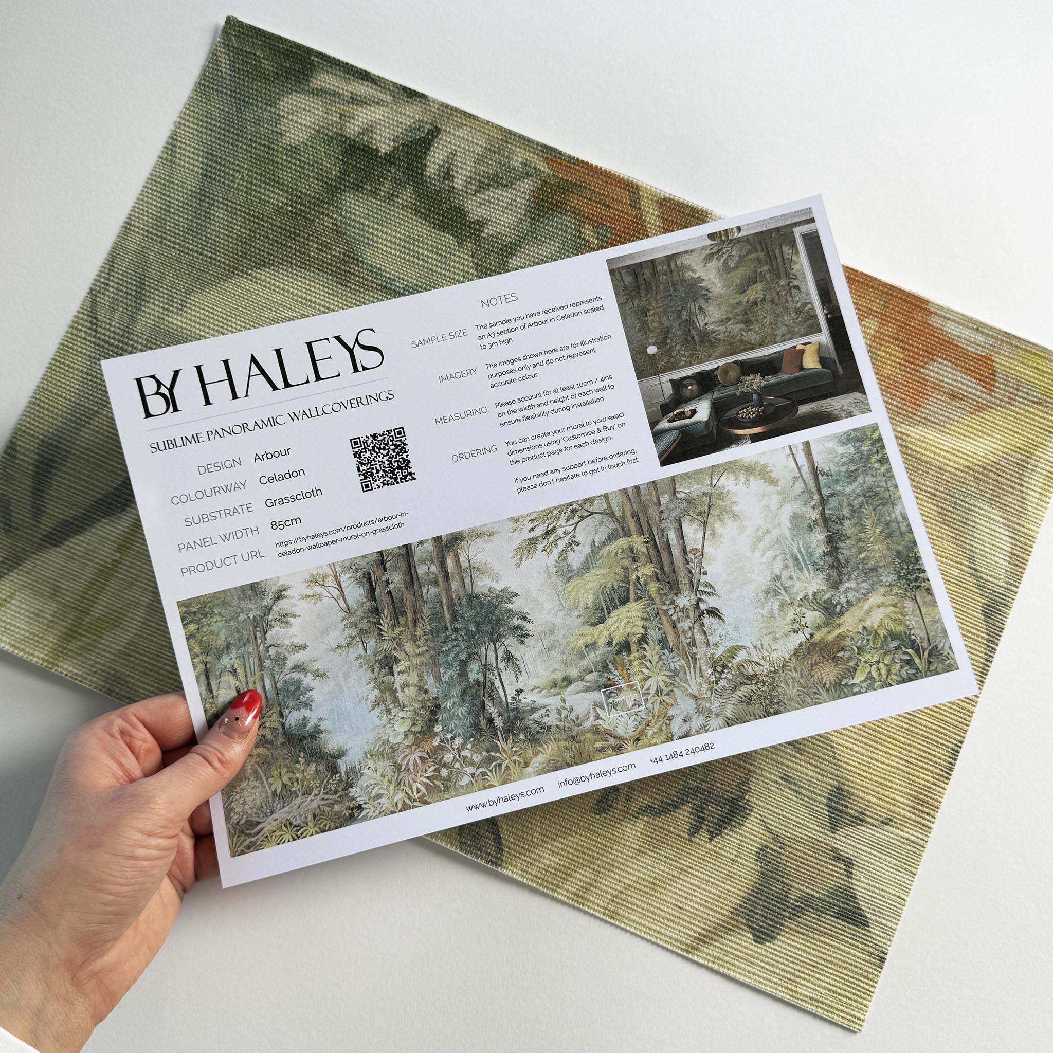 A hand showing information for a grasscloth wallpaper mural sample which features an airy woodland in sage, yellow, and mist.