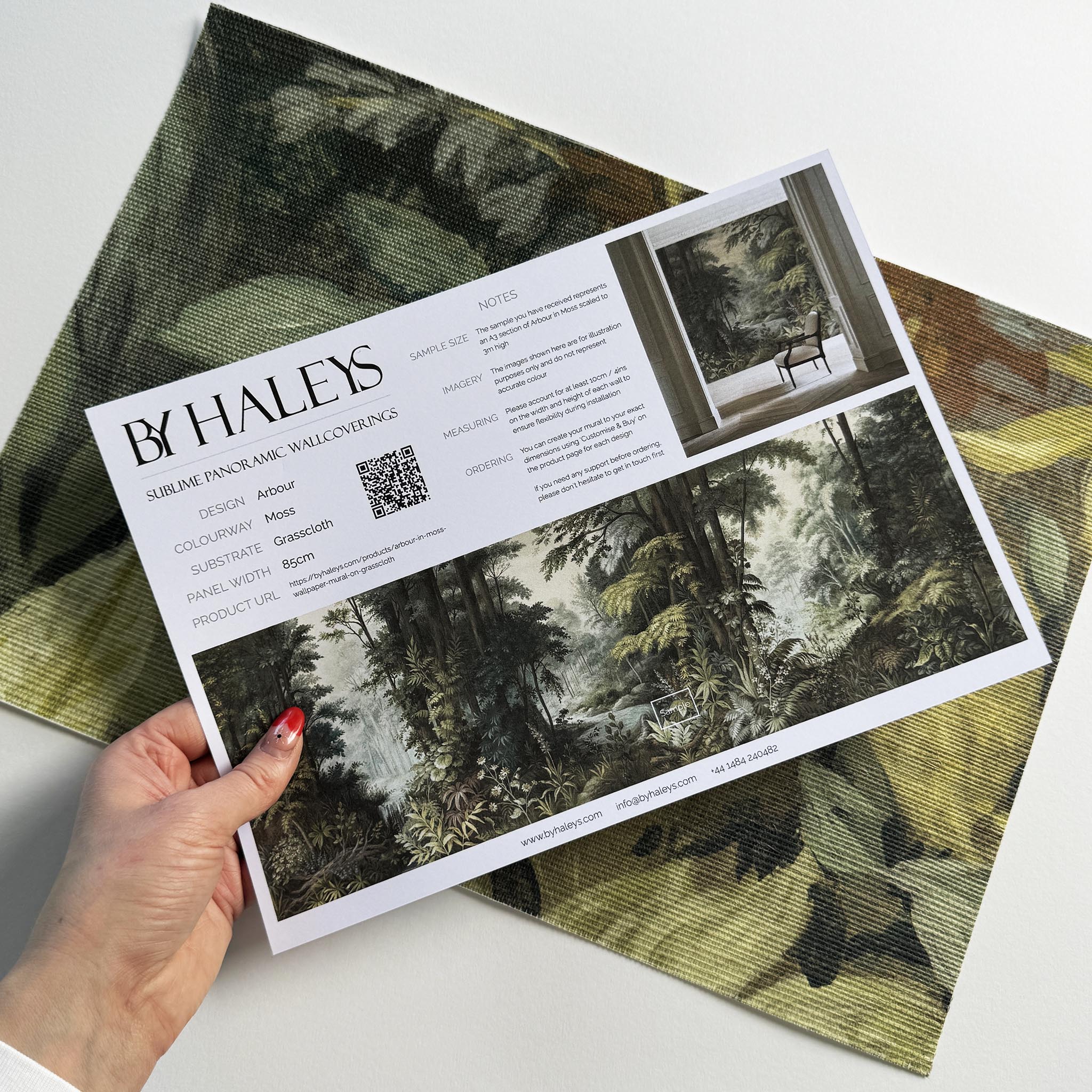 A hand showing information for a grasscloth wallpaper mural sample which features a misty woodland in sage and ochre.