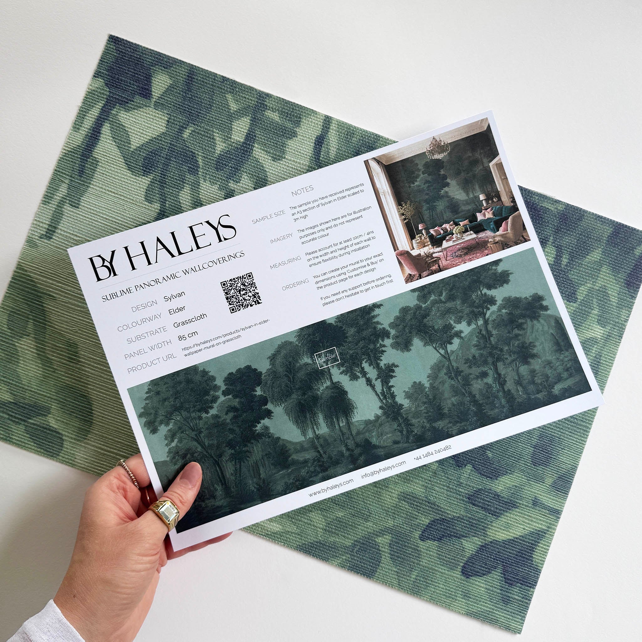 A hand showing information for a grasscloth wallpaper mural sample which features deep woodland