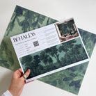 A hand showing information for a grasscloth wallpaper mural sample which features deep woodland
