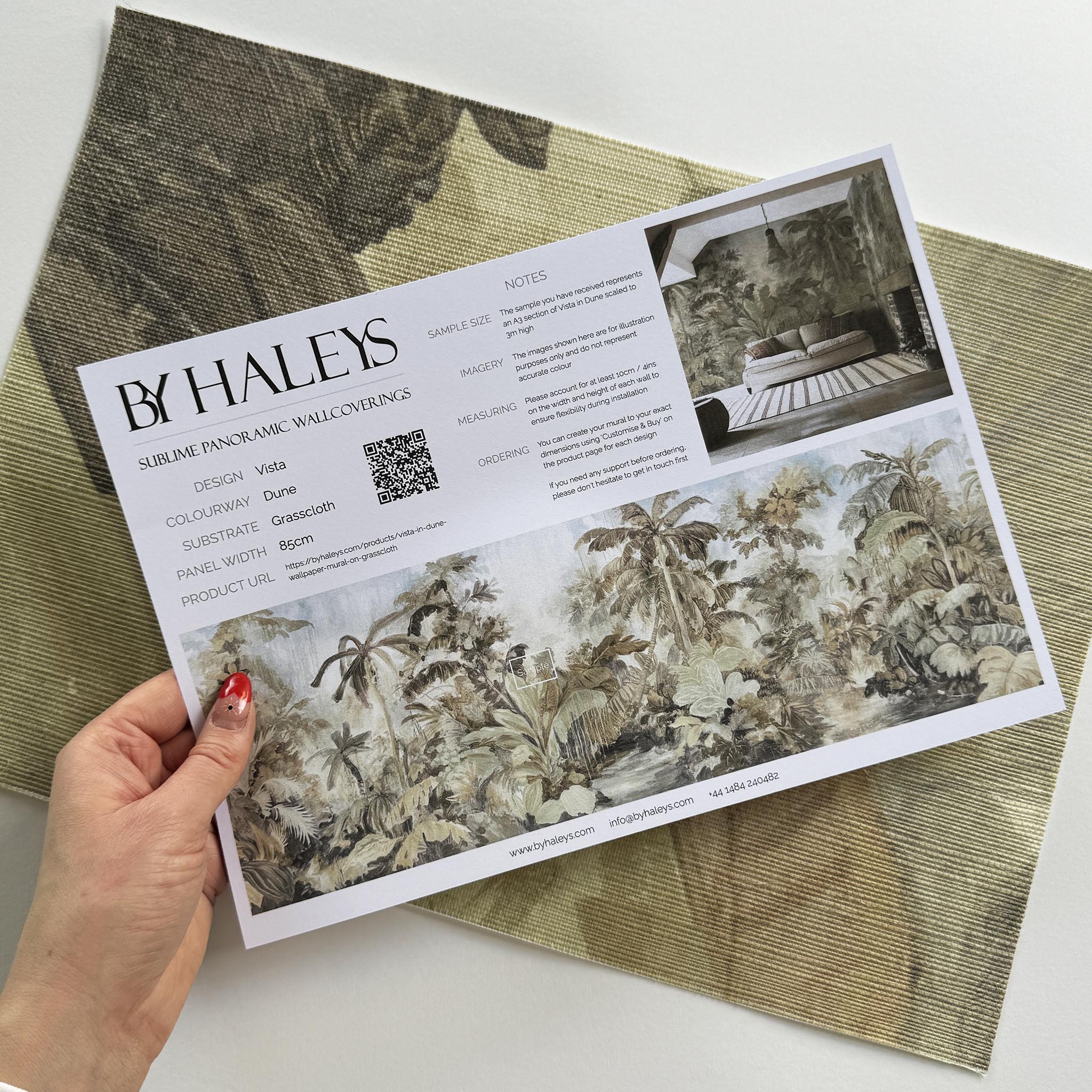 A hand showing information for a grasscloth wallpaper mural sample which features a jungle scene in sepia and blue.