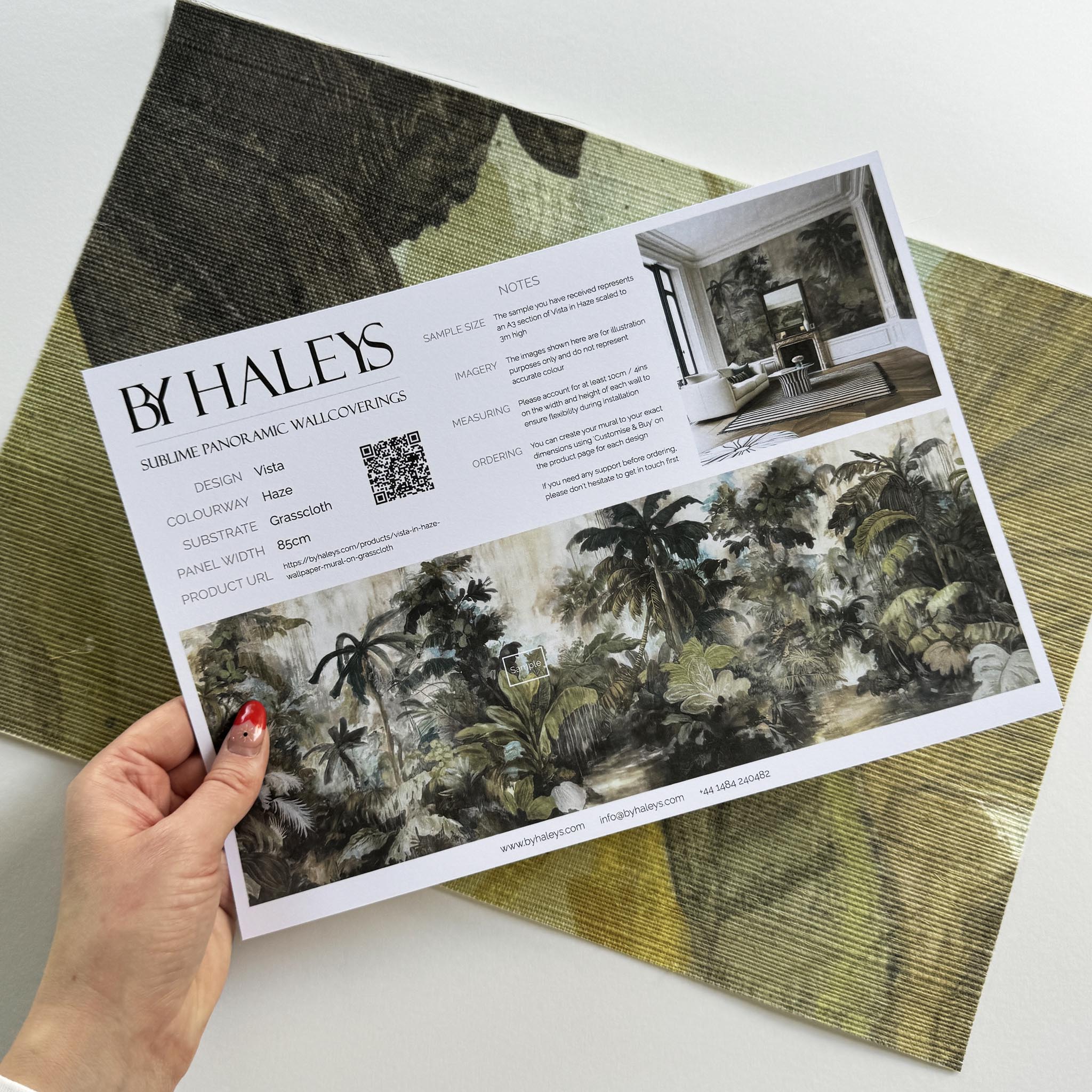 A hand showing information for a grasscloth wallpaper mural sample which features a tropical scene in sage and parchment.