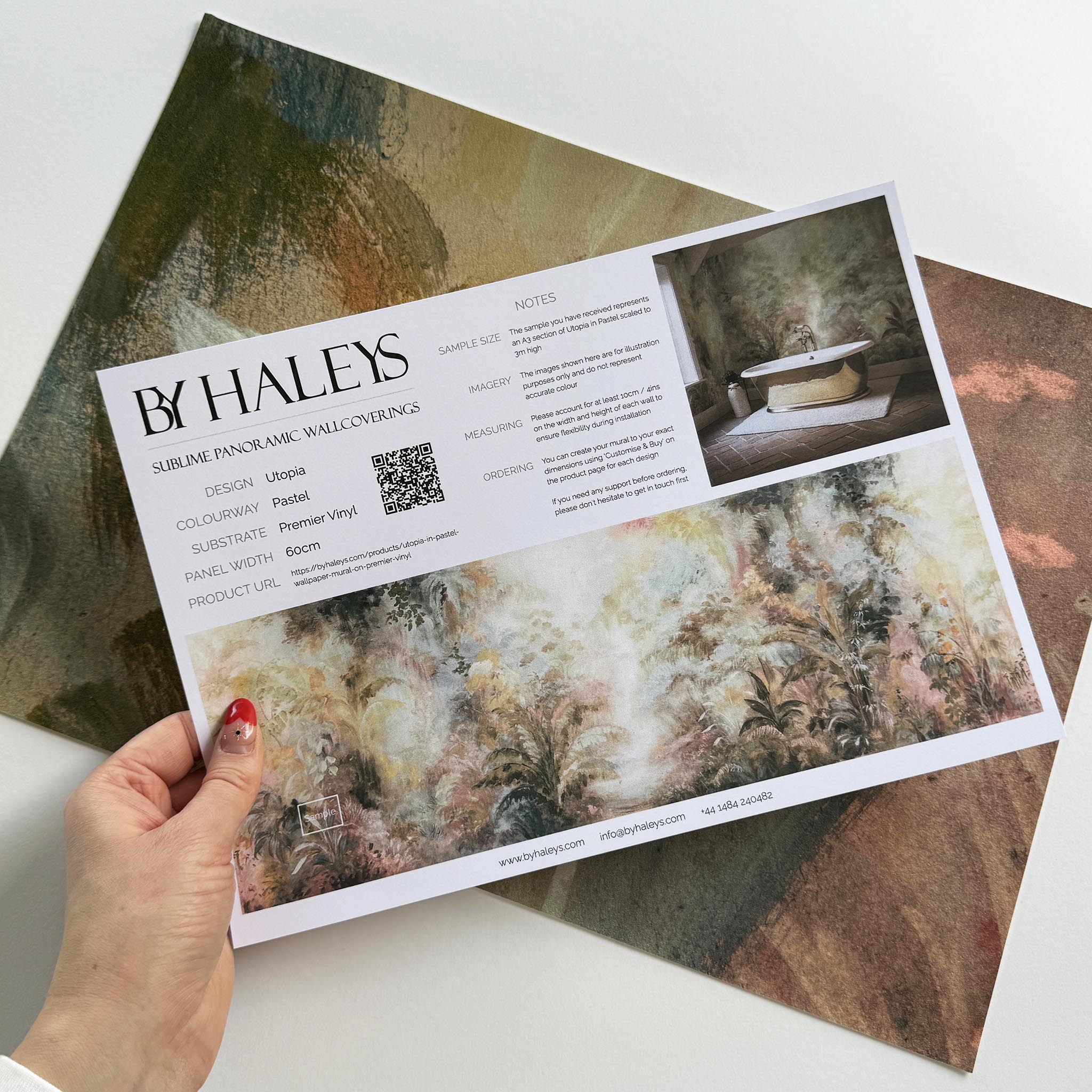 A hand showing information for a vinyl wallpaper mural sample which features a rainforest in blush and sky blue.