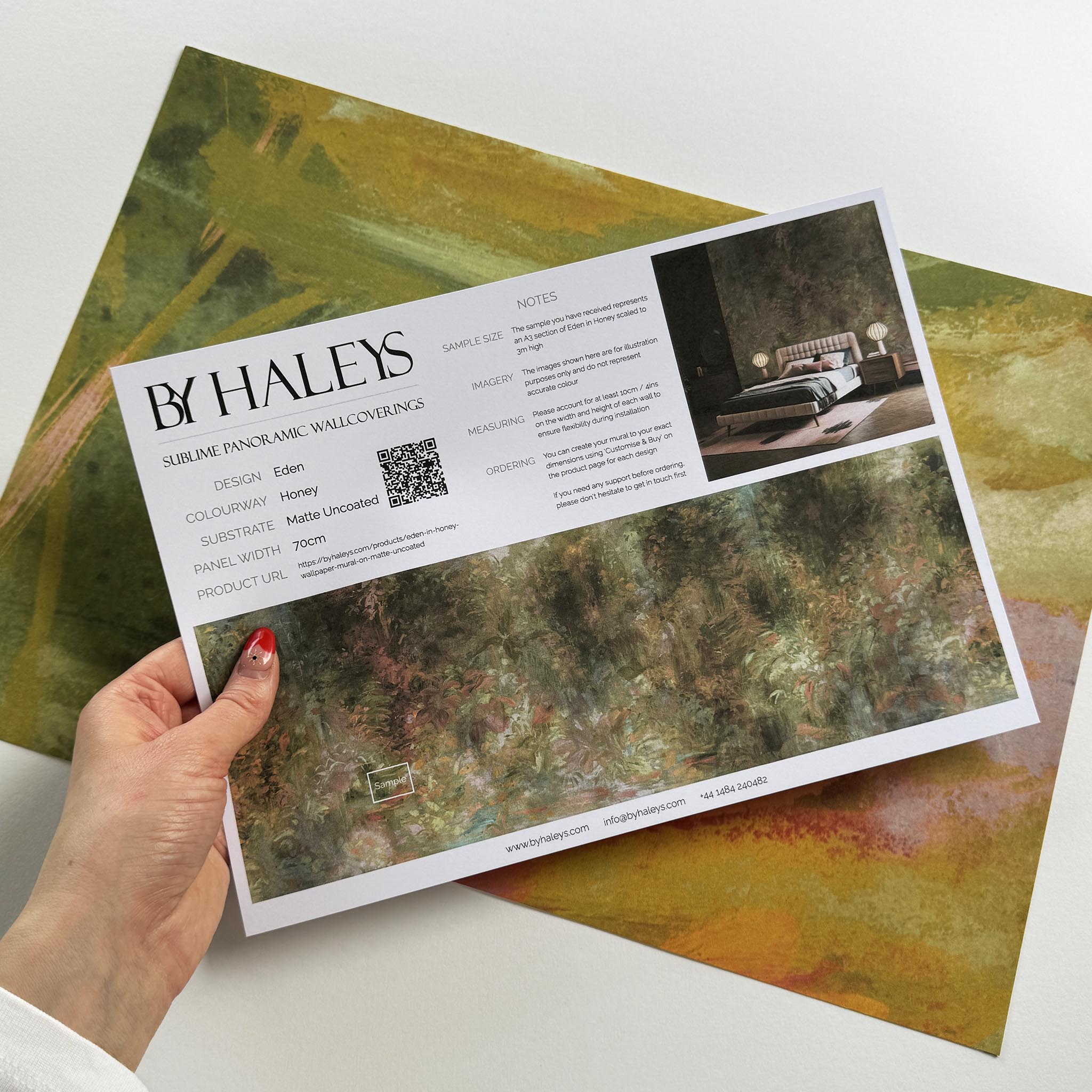 A hand showing information for a matte wallpaper mural sample which features a abstract layering of ochre and teal.
