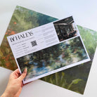 A hand showing information for a pearlescent wallpaper mural sample which features moody mural in nettle green, teal, ochre foliage.