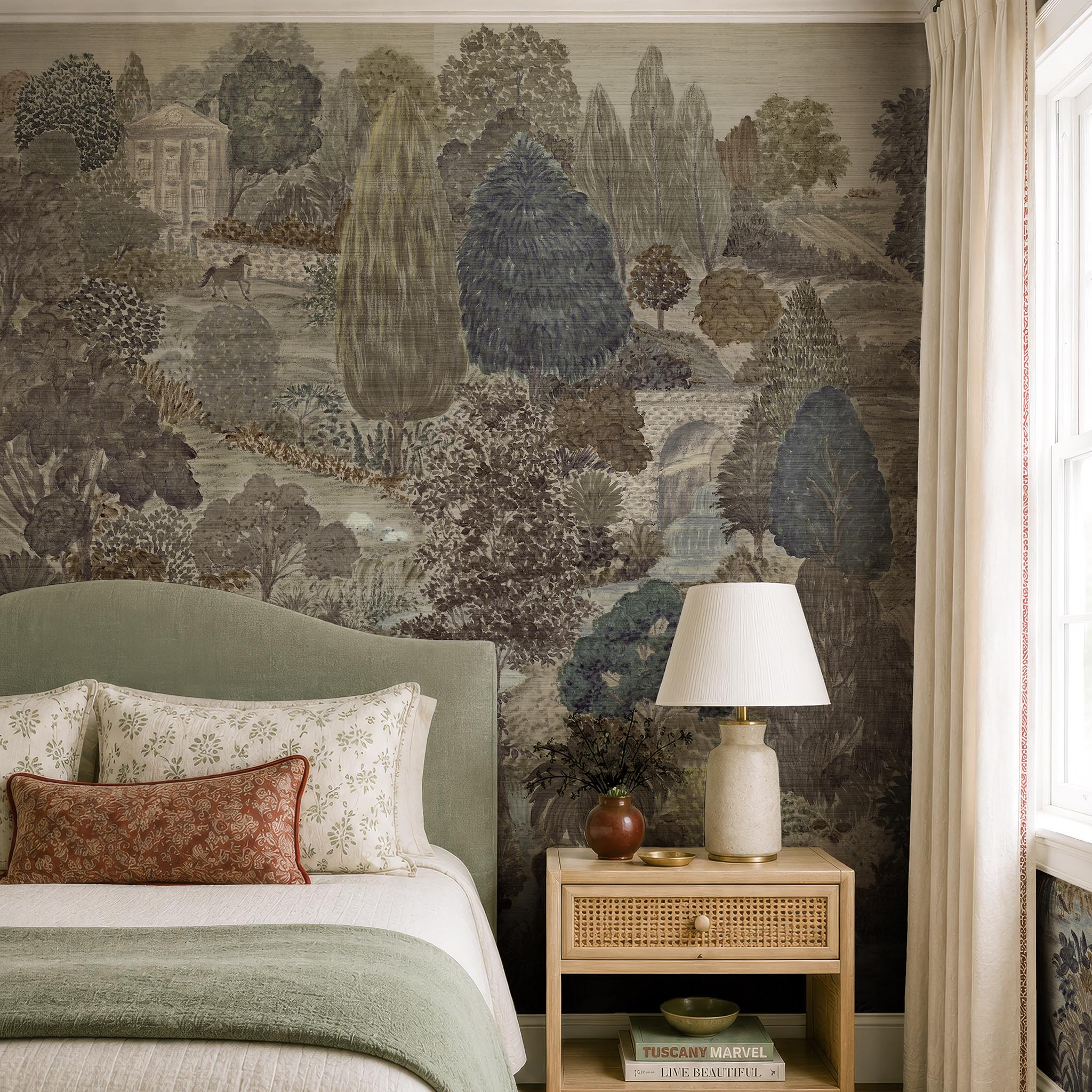 A cropped view of a bedroom featuring a panoramic grasscloth wallpaper mural of a countryside in deep olive, slate and ash