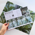 A hand showing information for a pearlescent wallpaper mural sample which features serene bergamot mural with celadon and sage tones.