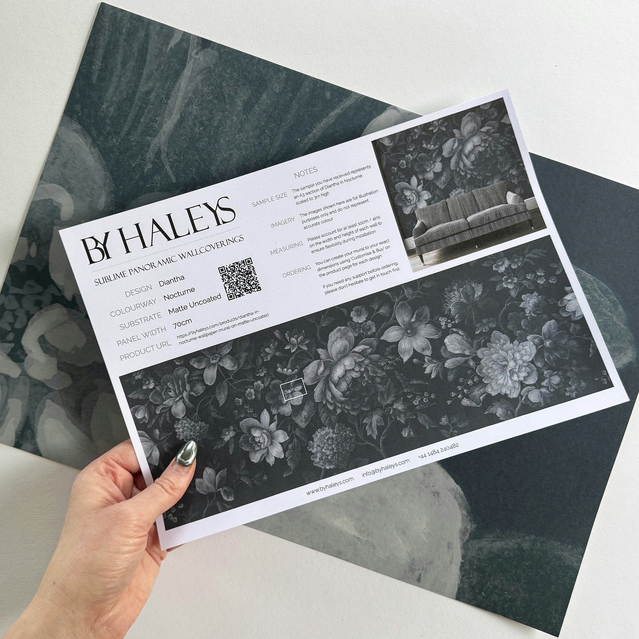 A hand showing information for a matte wallpaper mural sample which features moonlit florals on deep navy