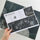 A hand showing information for a matte wallpaper mural sample which features moonlit florals on deep navy