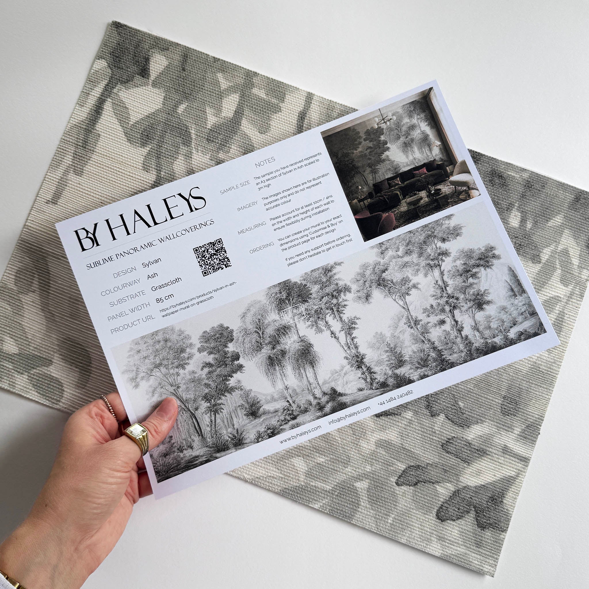 A hand showing information for a grasscloth wallpaper mural sample which features ash grey forest