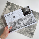 A hand showing information for a grasscloth wallpaper mural sample which features ash grey forest