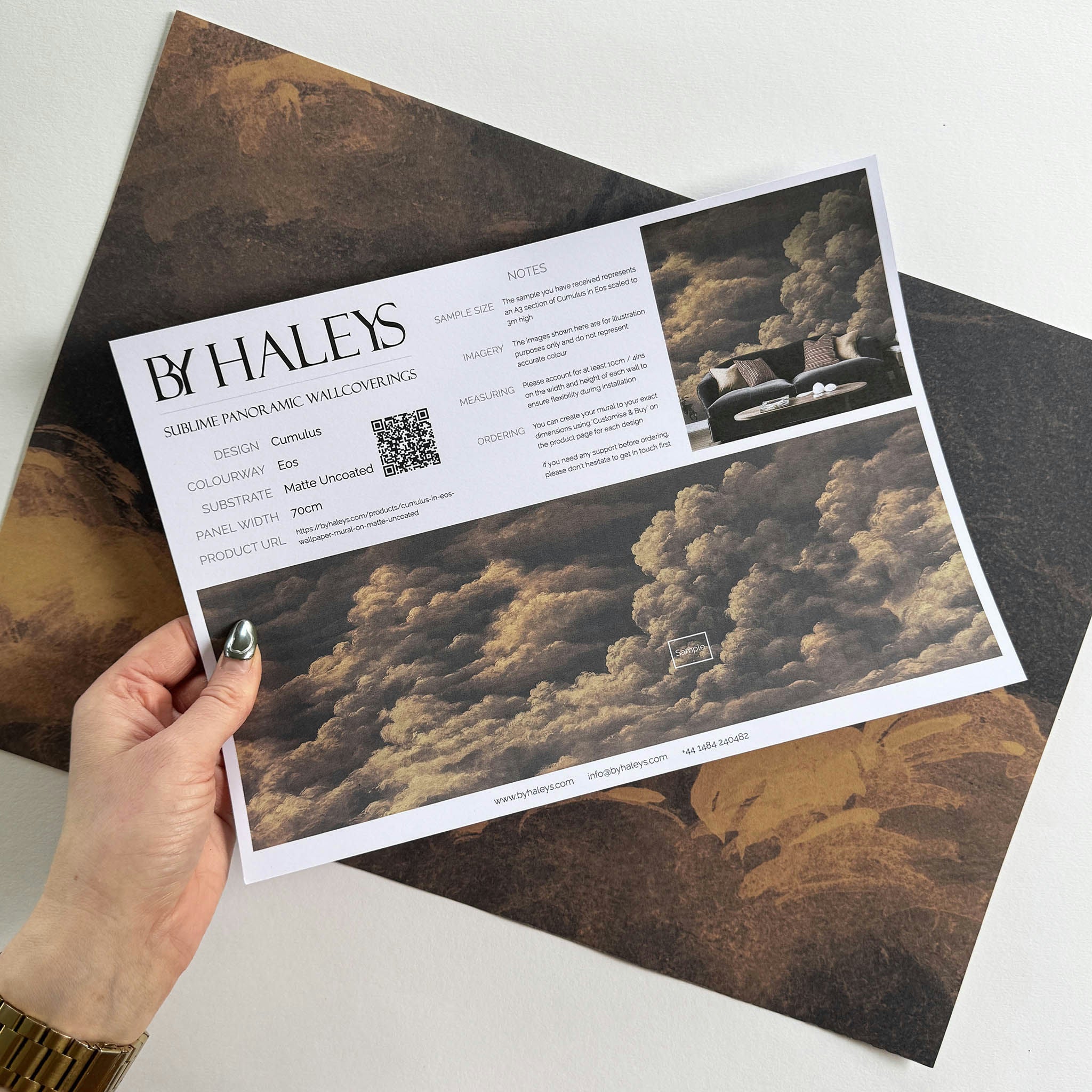 A hand showing information for a matte wallpaper mural sample which features warm peach clouds