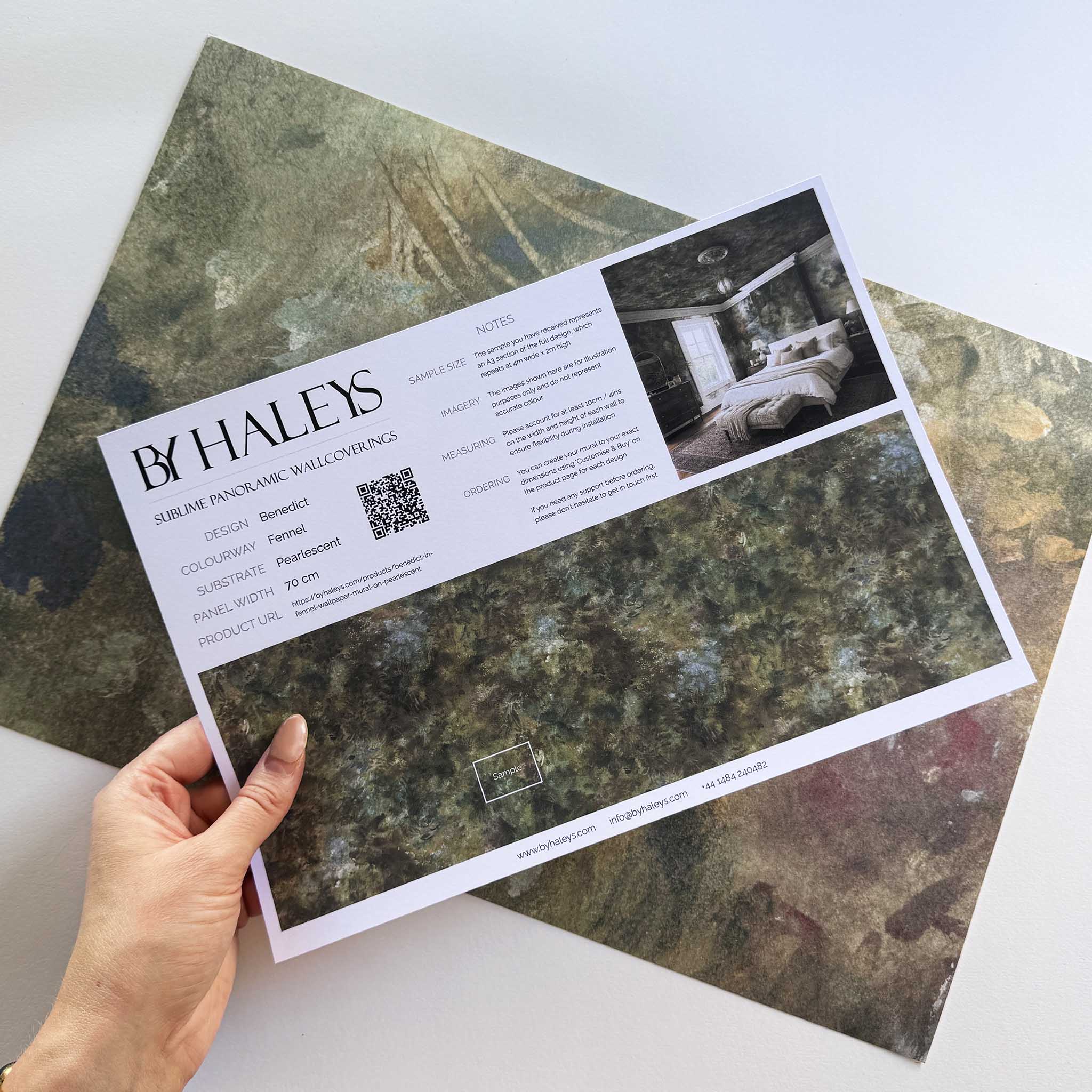 A hand showing information for a pearlescent wallpaper mural sample which features misty mural in fennel, sage, olive, indigo and ochre.