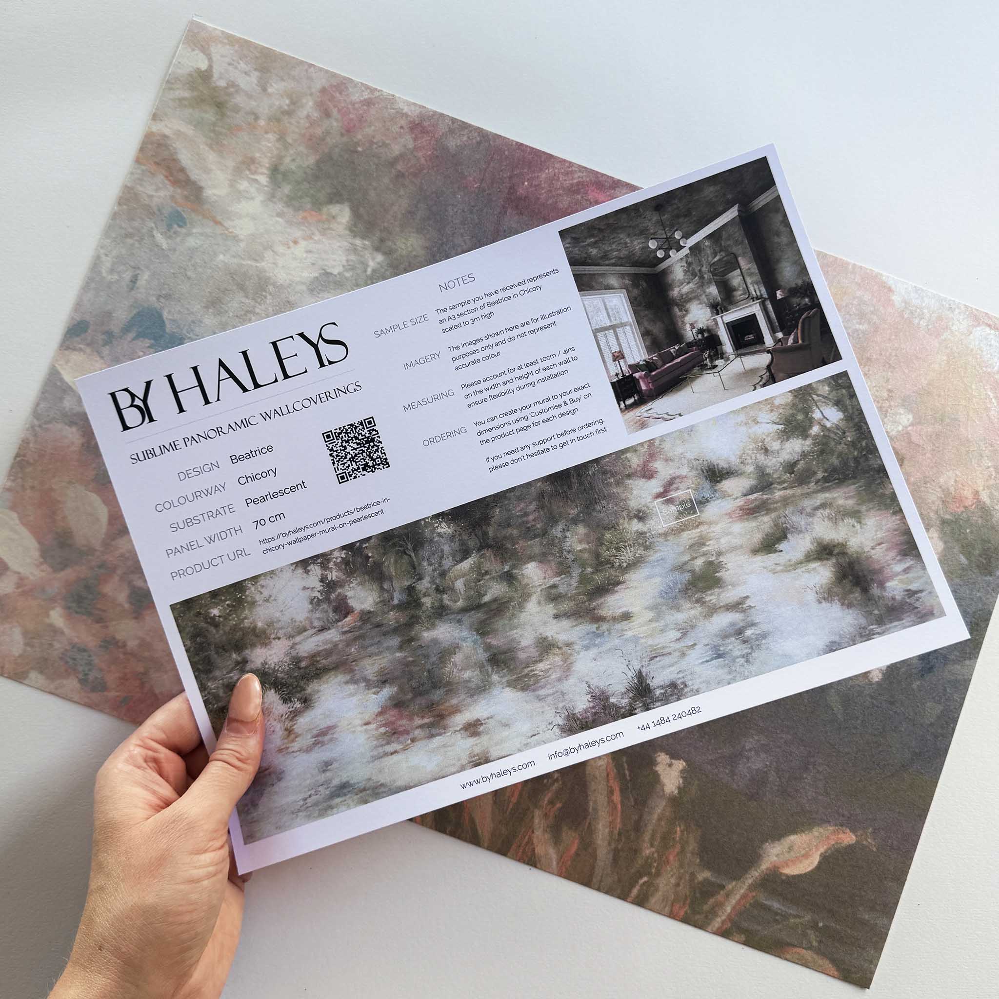 A hand showing information for a pearlescent wallpaper mural sample which features soft mural in chicory blue, dusty rose, sage and ochre.